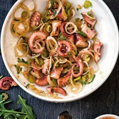 Un delicioso salpicón de pulpo con cebolla y perejil, servido en un plato blanco sobre una pizarra oscura.