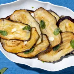Fette di melanzane grigliate, guarnite con menta fresca e aglio. Un contorno di verdure semplice e gustoso.