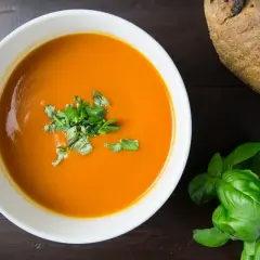 Pomidorowa zupa w misce, udekorowana bazylią, obok bochenek chleba. Zastanawiasz się, jak długo można przechowywać zupę w lodówce?