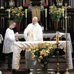 Ksiądz i ministrant podczas mszy świętej przy ołtarzu ozdobionym kwiatami.