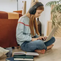 Dziewczynka w słuchawkach uczy się na laptopie, przygotowując argumenty, jak przekonać rodziców do szkoły w chmurze.