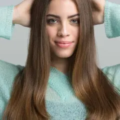 Joven sonríe con las manos en la cabeza, su cabello castaño cae sobre sus hombros. Apenas se notan las primeras canas, un toque de madurez.