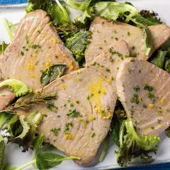 Fette di tonno al forno, profumate al limone e erbe aromatiche, servite su un letto di insalata fresca.