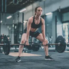 Femme concentrée en position pour un soulevé de terre, haltères lourds prêts à être soulevés dans une salle de sport.
