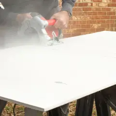 A person demonstrates how to cut cement board with a circular saw, creating a cloud of dust.