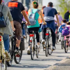 Grupa rowerzystów jedzie w kolumnie, przestrzegając przepisów. Widać plecaki i odblaskowe kamizelki.
