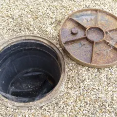 Un regard sur une canalisation d'eau pluviale ouverte, prête à être débouchée. Le couvercle rouillé est à côté.