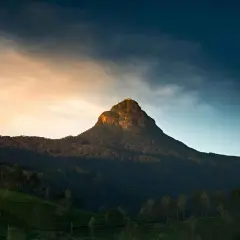 Adam's Peak reser sig majestätiskt mot en dramatisk himmel. Bergssluttningarna är täckta av frodig grönska och teodlingar.
