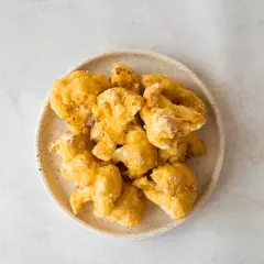 Alitas de coliflor doradas y crujientes en un plato, listas para disfrutar.