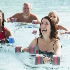 Personas sonriendo y haciendo aqua gym en una piscina con pesas flotantes.