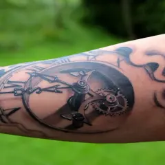 Tatuaż na piszczelu przedstawia mechanizm zegara z rzymskimi cyframi i dymem.