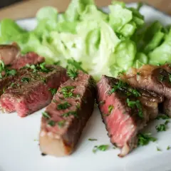 Tranches de steak black angus saignant, garnies de persil frais, servies avec de la laitue croquante sur une assiette blanche.