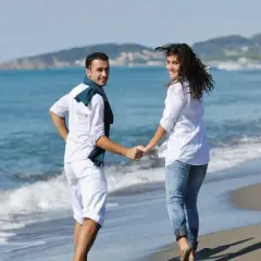 Para na plaży, trzymając się za ręce, cieszy się majówką. Słońce, morze i góry w tle tworzą idealny krajobraz.