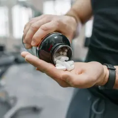 Mann schüttet weiße Pillen aus einer Flasche in seine Hand. Möglicherweise zur Unterstützung der Yohimbin Wirkung im Fitnessstudio.
