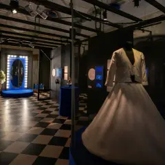 En vit dansklänning visas upp i en monter på Dansmuseet Stockholm. Golvet har ett schackrutigt mönster.