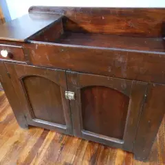 A vintage wooden dry sink with a drawer and cabinet doors, perfect for a rustic kitchen or bathroom.