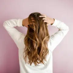 Mujer con pelos largos y ondulados, de color castaño, jugando con su cabello.