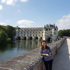 Kobieta na tle zamku Chenonceau nad rzeką w słoneczny dzień.