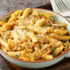 Makaron penne z karmelizowaną cebulą i roztopionym serem, ozdobiony tymiankiem.