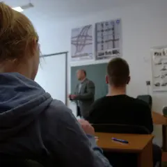 Uczniowie na kursie prawa jazdy, zastanawiają się, ile przed 18 można zdawać egzamin teoretyczny. Na ścianie znaki drogowe.