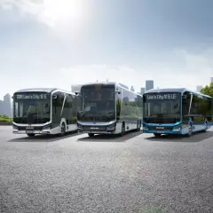 Trzy nowoczesne autobusy elektryczne MAN Lion's City E stoją na tle miejskiej panoramy.