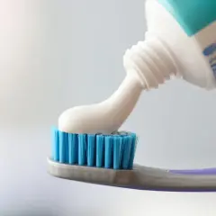 Pasta do zębów z fluorkiem cyny nakładana na niebieską szczoteczkę.