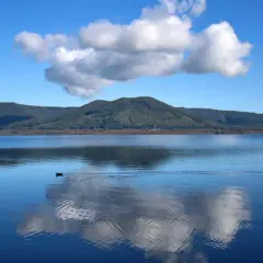 Un'oasi di pace al lago di Vici, con un cielo azzurro punteggiato da nuvole bianche che si specchiano sull'acqua calma.