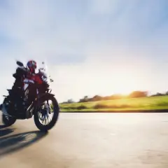 Motocyklista w kasku pędzi drogą, ciesząc się pięknym zachodem słońca. To idealny **sezon motocyklowy**!