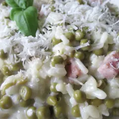 Creamy risotto with peas, ham, and grated cheese, garnished with a basil leaf.