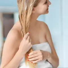 Kobieta z blond włosami nakłada domową odżywkę do włosów, która nadaje im blask i miękkość.