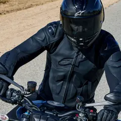 Motocyklista w kasku i czarnej kurtce Alpinestars jedzie po pustynnej drodze.