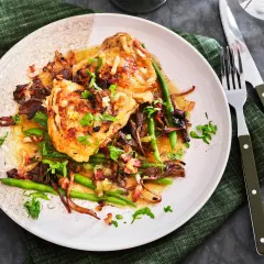 En tallrik med kyckling i vitvinssås, svamp, haricots verts och bacon. En utsökt coq au vin blanc.