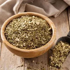 Suszone liście yerba mate w drewnianej misce i szufelce. Choć yerba mate ma wiele zalet, warto pamiętać o jej negatywnych właściwościach, np. o zawartości kofeiny.