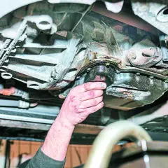 Mano revisa el cárter de un coche, mostrando signos de perdida de aceite.