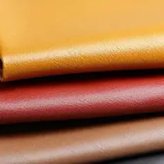 Pile de cuirs enduits aux couleurs vives : jaune, rouge, marron et noir. Ce cuir enduit, c'est quoi ? Une matière synthétique résistante et polyvalente.