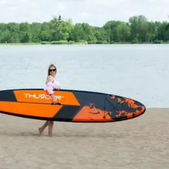 Kobieta z pomarańczowo-czarnymi deskami do pływania z wiosłem na piaszczystej plaży, gotowa do wodnych przygód.