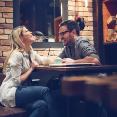 Para śmieje się podczas randki w kawiarni przy stoliku z napojami.