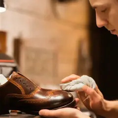 Un artisan applique du cirage pour chaussures sur un soulier en cuir marron, lui redonnant son éclat.