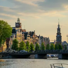 Złota godzina nad kanałem, gdzie jest Amsterdam. Wąskie kamienice, most pełen rowerów i łodzie na wodzie.
