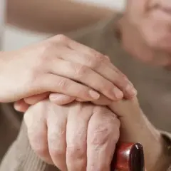 Dłoń opiekunki na dłoni starszego mężczyzny, który trzyma laskę. Wsparcie i troska, jak przy leczeniu np. chorobą Parkinsona, gdzie **Madopar** może pomóc.