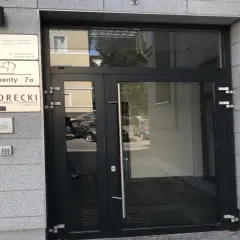 Drzwi wejściowe do budynku z tabliczkami informacyjnymi, w tym "SKORECKI KANCELARIA DORADCY FINANSOWEGO".