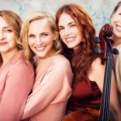 Vier lächelnde Frauen, eine davon hält ein Cello. Salut salon mitglieder, bereit für den Auftritt.