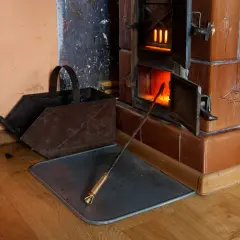 Piec kaflowy z otwartym paleniskiem, żarem i pogrzebaczem. Obok stoi metalowy kosz na węgiel. Pytanie: czy ekogroszkiem można palić w piecu kaflowym?