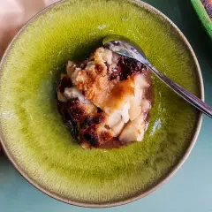 Un délicieux crumble poire chocolat, doré et croustillant, servi dans une assiette verte avec une cuillère.
