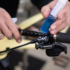 Hands add blue brake fluid from a syringe to a bicycle brake lever. This fluid is corrosive due to its hygroscopic nature, absorbing moisture.