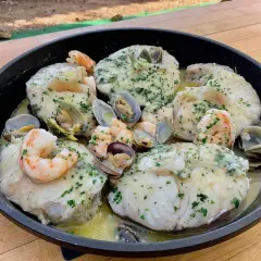 Merluza con almejas y gambas en una sartén, con perejil picado y salsa cremosa. ¡Un plato marinero delicioso!