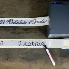 Taśma z napisem "W Ostatniej Drodze" przygotowywana do wieńca. Wzór jest elegancki i symboliczny.