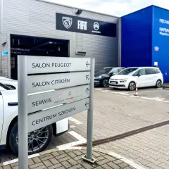 Znak z napisem "Salon Peugeot", "Salon Citroën", "Serwis" i "Centrum Szkoleń" przy salonie samochodowym. ASO skrót.