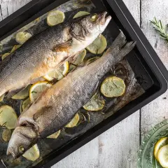 Due branzini al forno su teglia con patate, limone e rosmarino. Un piatto semplice e gustoso pronto per essere servito.