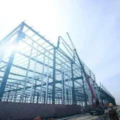 Budowa hali z konstrukcji stalowej. Widać dźwig i robotników. Ceny stali zbrojeniowej wpływają na koszty inwestycji.